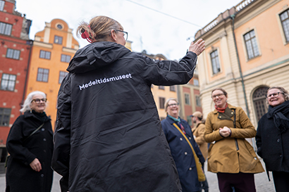 En grupp människor står samlade på Stortorget i Gamla stan och lyssnar på en guide.